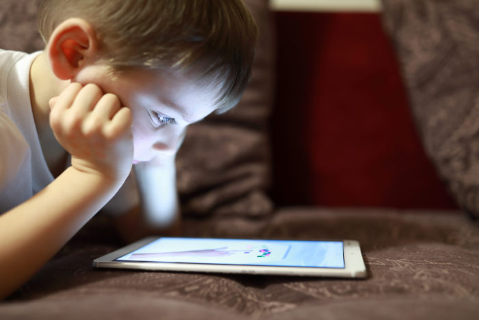Un enfant regarde une tablette, couché sur un canapé